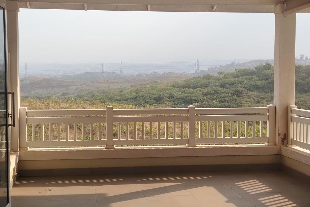 A spacious covered balcony featuring tiled flooring and a protective railing, offering expansive views of the surrounding landscape.