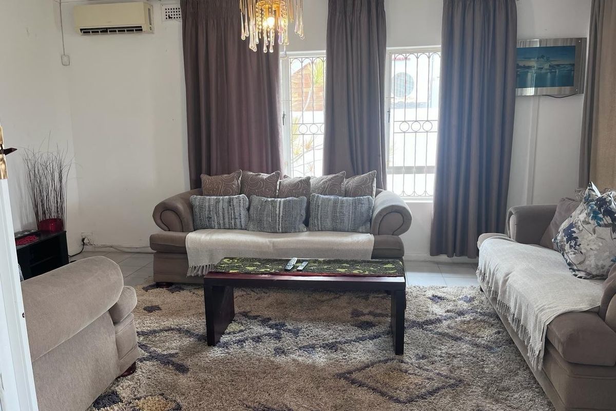 A comfortable living room featuring an air conditioning unit, security bars on the windows, and a decorative chandelier.