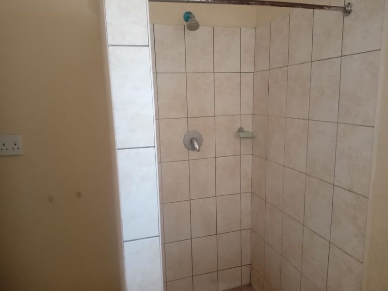 A functional shower enclosure featuring neutral wall tiles, a standard shower head, and a built-in soap dish.