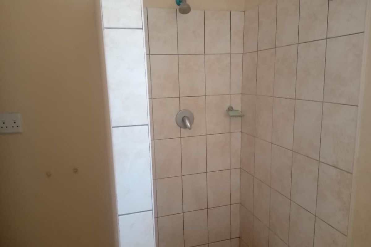 A functional shower enclosure featuring neutral wall tiles, a standard shower head, and a built-in soap dish.