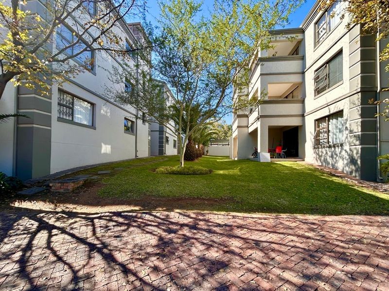A view of the rear exterior of the apartment complex, featuring a well-maintained lawn, paved driveway, and private balconies.