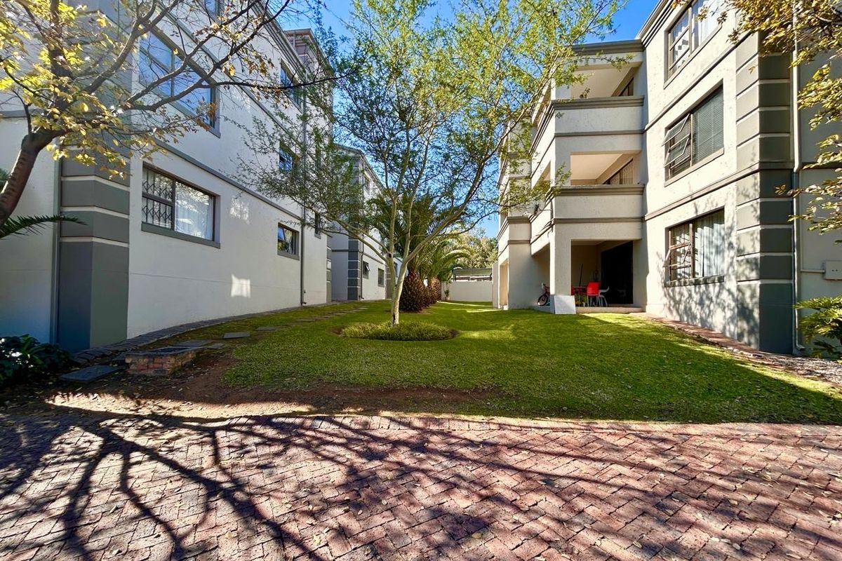 A view of the rear exterior of the apartment complex, featuring a well-maintained lawn, paved driveway, and private balconies.