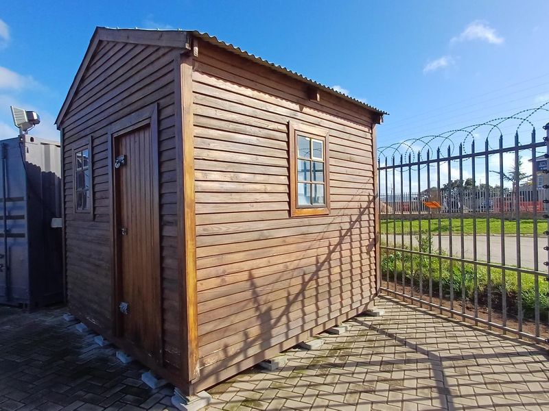 A well-maintained timber utility shed situated on a paved industrial site, secured by perimeter fencing.