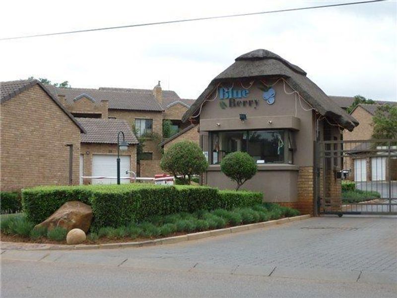 The entrance to the Blue Berry complex featuring a security guard house with a thatch roof, paved driveway, and controlled access gate.