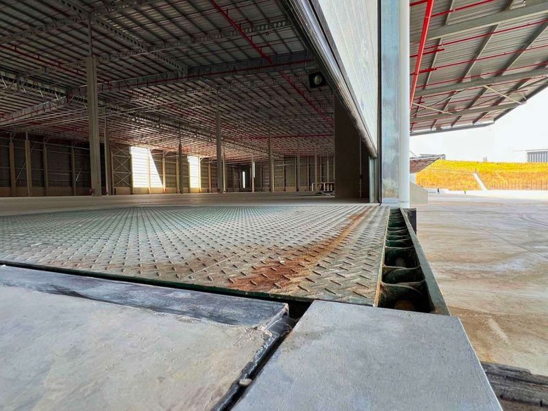Industrial warehouse interior featuring a large open floor plan, exposed steel structure, fire sprinkler system, and a dock leveller at the loading bay entrance.