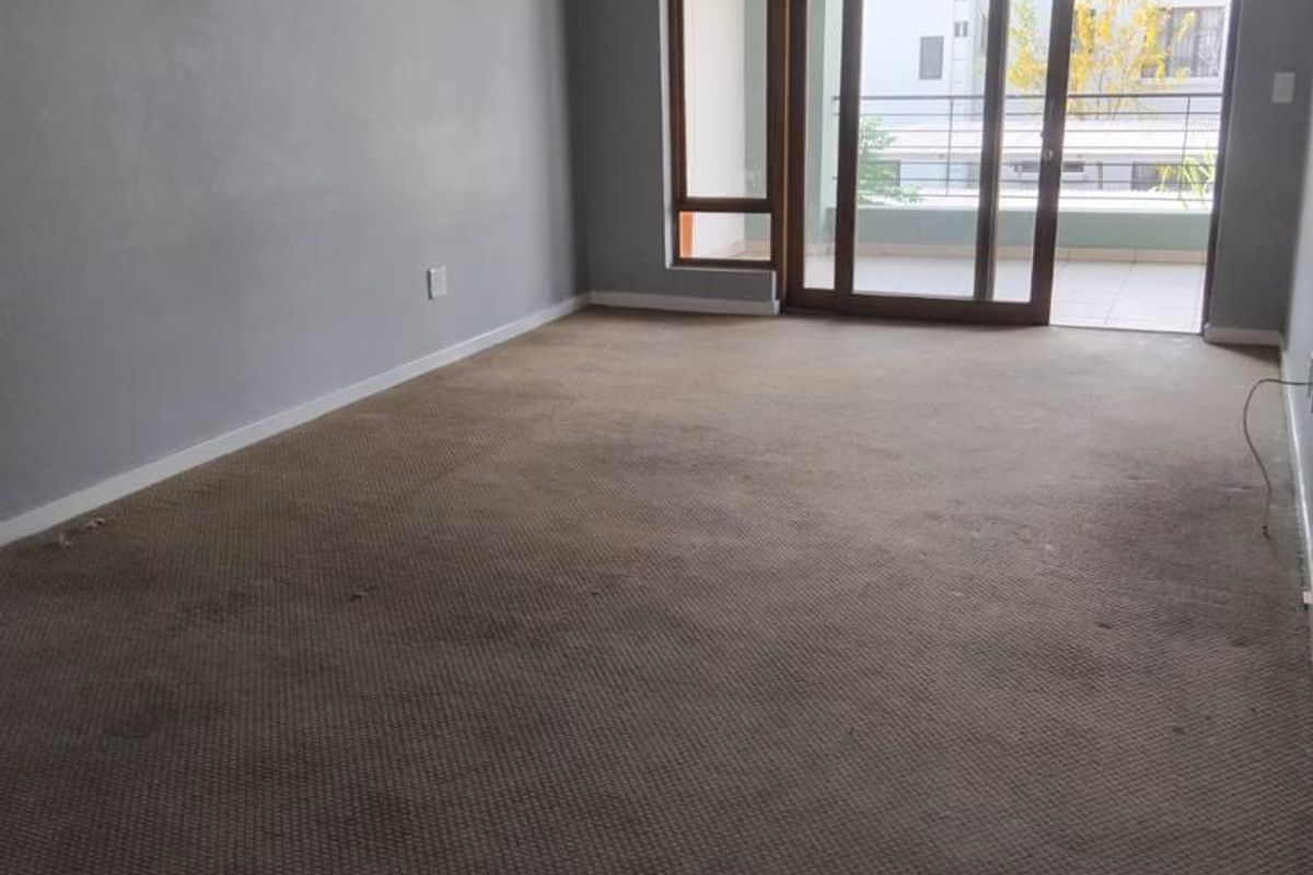 Spacious living area featuring neutral grey walls, carpeted flooring, and large sliding glass doors providing access to an attached balcony.