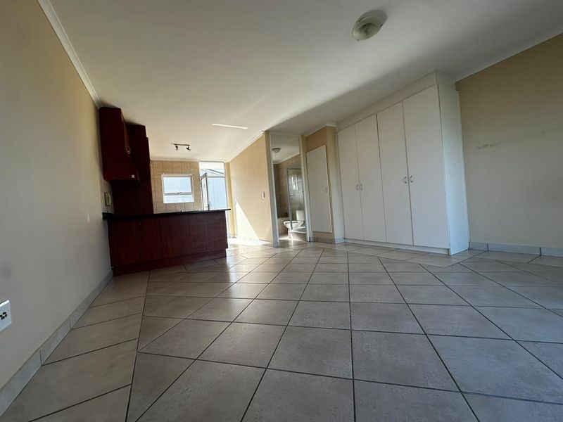 An open-plan living area featuring tiled flooring, built-in storage cupboards, and a compact kitchen space, presenting a clean, vacant canvas for potential residents.