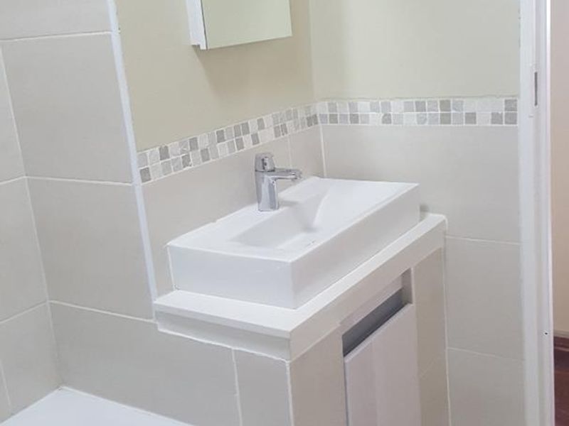 A clean, neutral-toned bathroom featuring a modern basin with a mixer tap, built-in vanity, and a bathtub with tiled finishes.