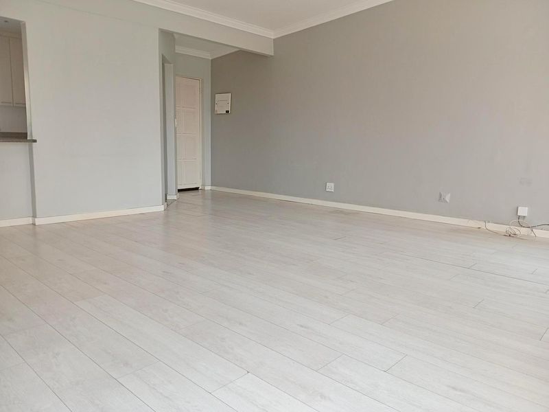 A spacious, empty living area featuring light-toned laminate flooring, neutral grey walls, and classic coving detail.