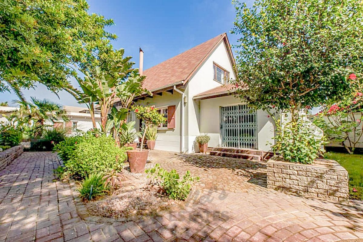 A charming rear exterior view featuring a paved patio area, established garden landscaping, and a white building facade with a pitched roof.