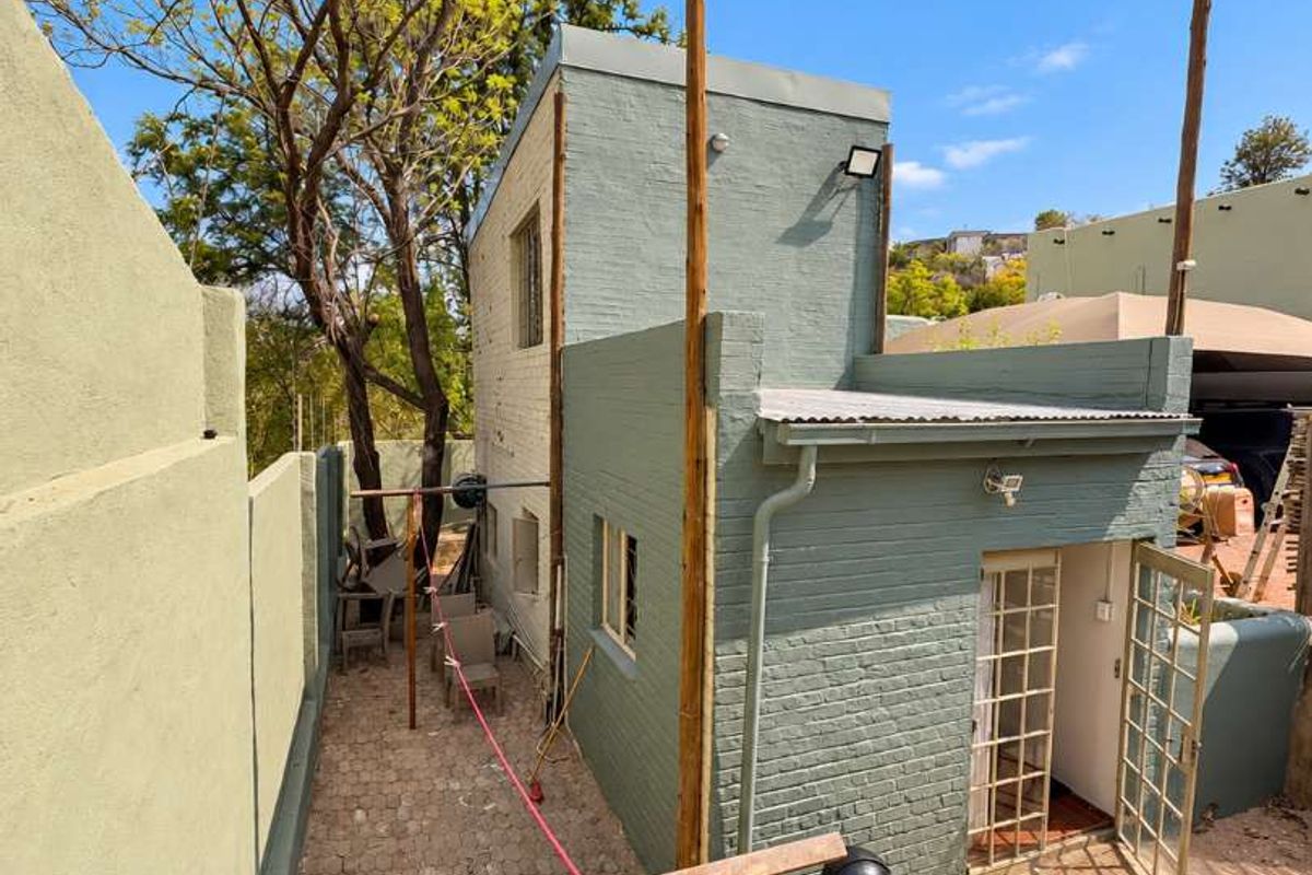 Rear exterior view of the property featuring painted brick walls, paved ground, and a security gate entrance.