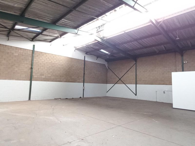 Spacious industrial warehouse unit featuring high ceilings, exposed steel trusses, concrete flooring, and blockwork walls, suitable for storage or light manufacturing operations.