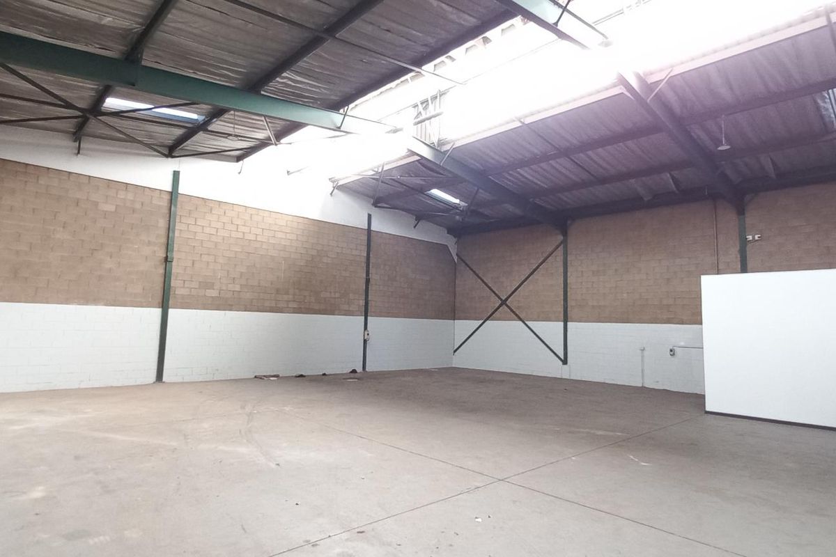 Spacious industrial warehouse unit featuring high ceilings, exposed steel trusses, concrete flooring, and blockwork walls, suitable for storage or light manufacturing operations.