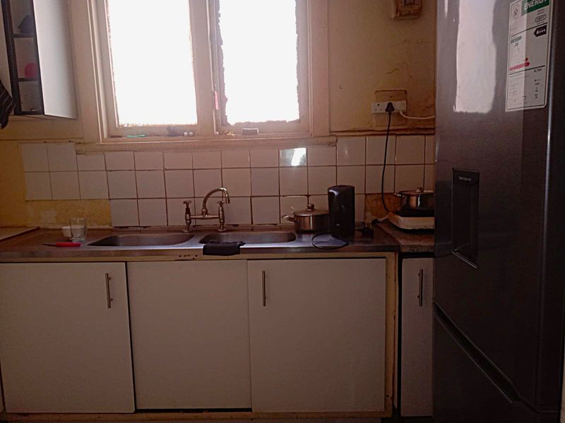 A dated kitchen area featuring a double basin sink, tiled splashback, and laminate countertops, requiring cosmetic updates and repairs to wall finishes.