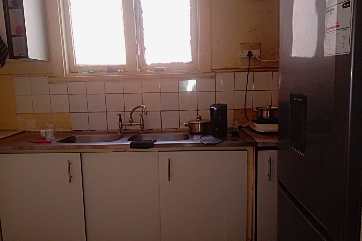 A dated kitchen area featuring a double basin sink, tiled splashback, and laminate countertops, requiring cosmetic updates and repairs to wall finishes.