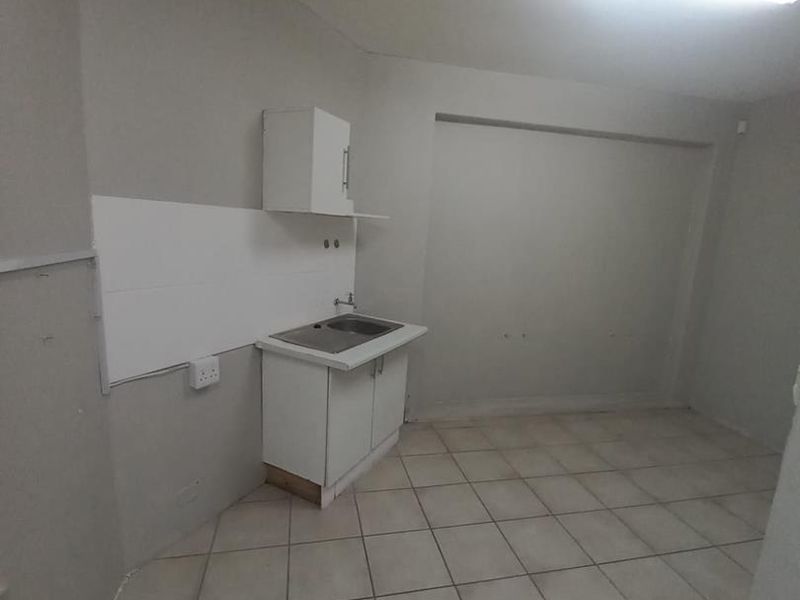 A compact, empty kitchen area featuring basic cabinetry, a single sink, tiled flooring, and a tiled splashback, requiring cosmetic updates.