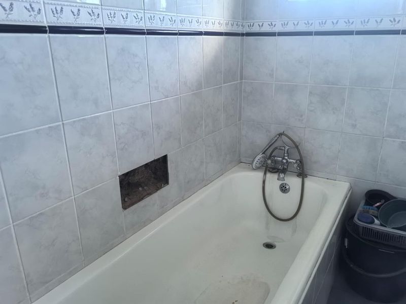 A bathroom featuring a standard bathtub with a shower mixer and tiled walls, currently showing a missing tile and exposed wall cavity.