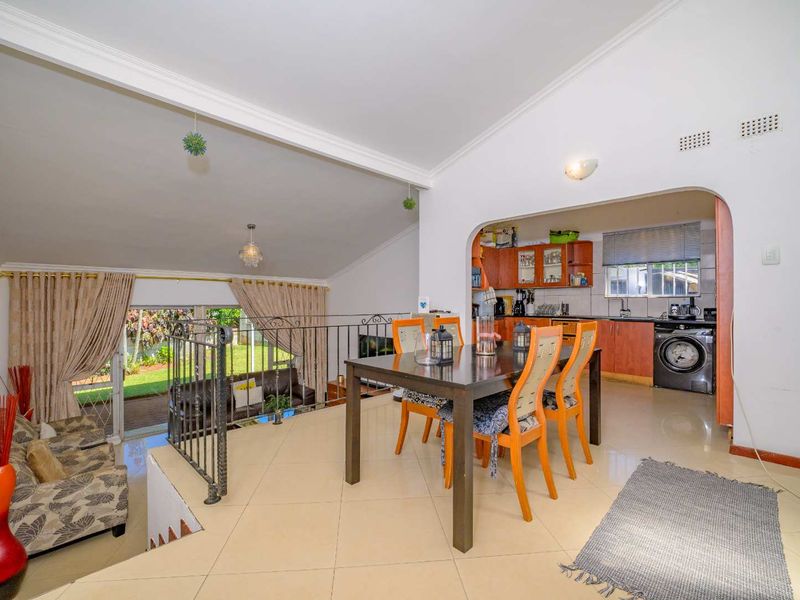 Open-plan living and dining area featuring tiled floors, a vaulted ceiling, and a connected kitchen with built-in cabinetry and direct access to the garden.