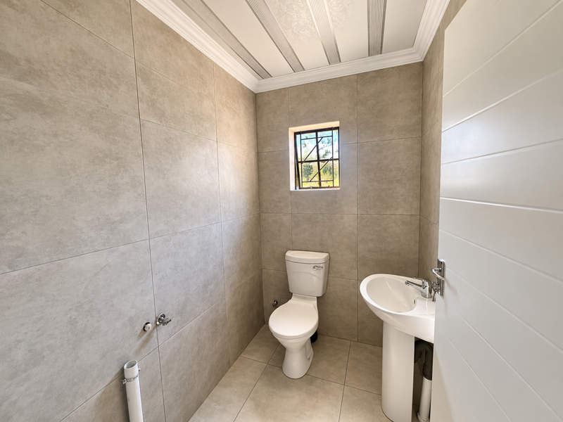 A clean, modern bathroom featuring neutral floor-to-ceiling tiling, a pedestal basin, and a standard toilet, offering a bright and functional space.