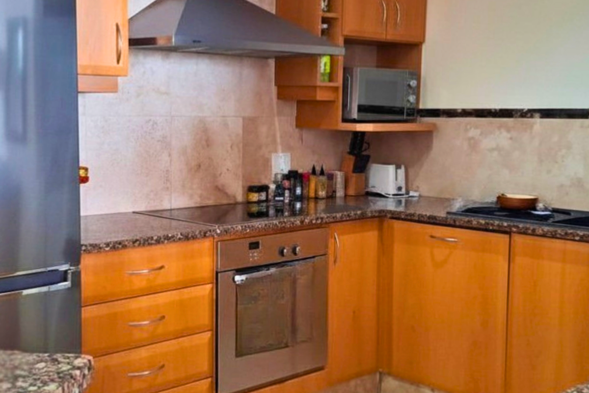 A functional kitchen featuring wooden cabinetry, granite countertops, a built-in oven, electric hob, and a stainless steel extractor fan.