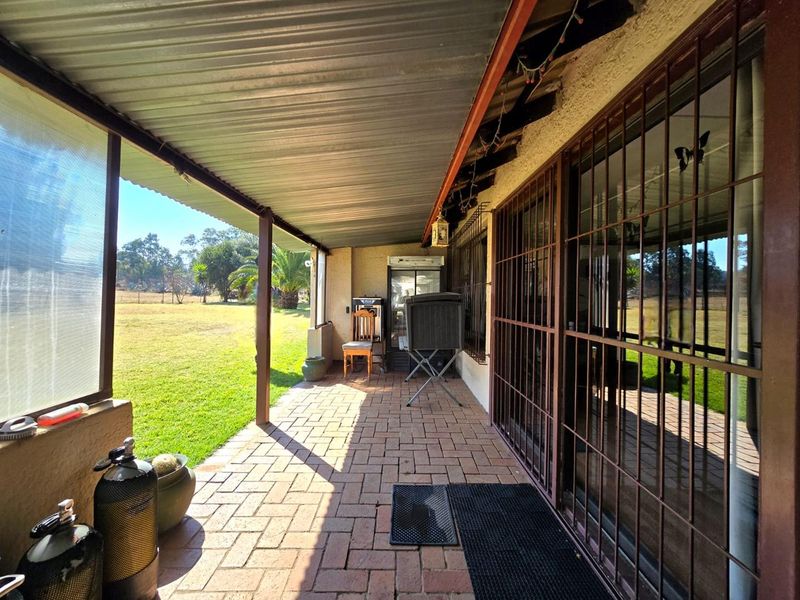 A covered patio area featuring brick paving, corrugated metal roofing, and security-barred sliding doors, overlooking the property's garden space.
