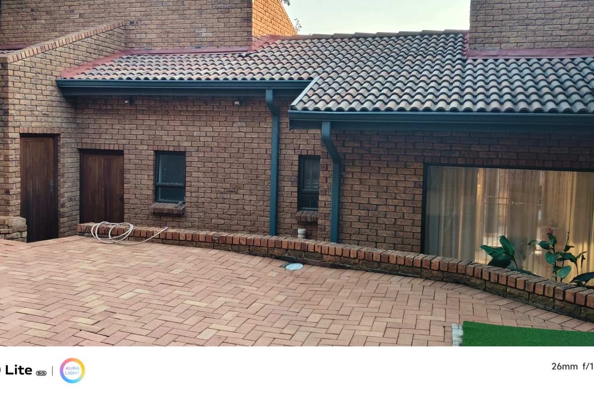 A rear exterior view of the house featuring face-brick walls, a tiled roof, and a paved patio area.