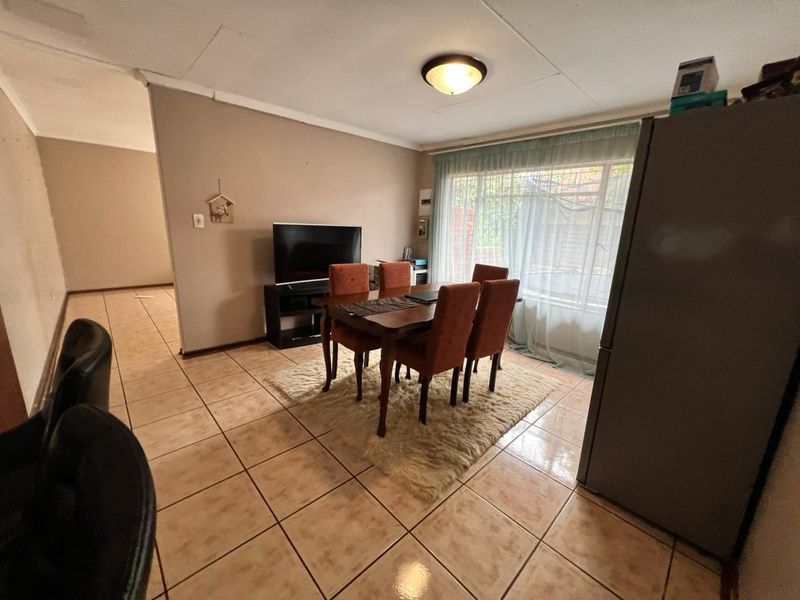 Dining area featuring ceramic floor tiles, a large window with sheer curtains, and a central ceiling light fixture.