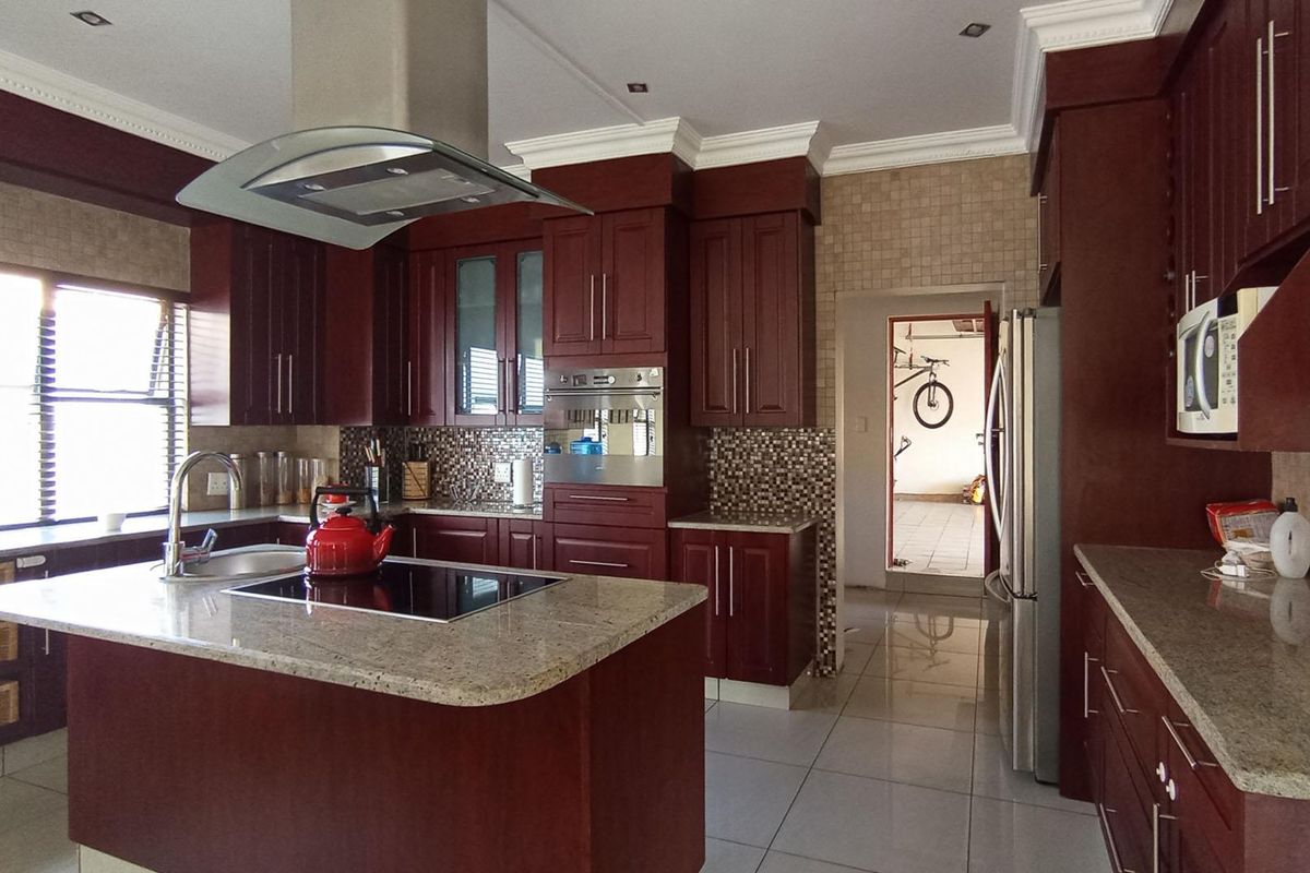 A well-appointed kitchen featuring dark wood cabinetry, granite countertops, a central island with a built-in hob, and a stainless steel extractor fan.