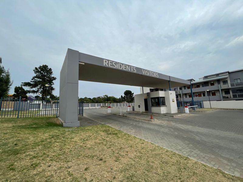 The main entrance to the apartment complex featuring a secure gatehouse, boom gate access, and paved driveway.