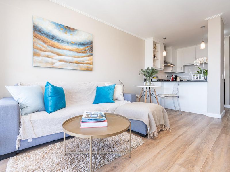 An open-plan living area featuring laminate flooring and a modern kitchen with white cabinetry and stone countertops.