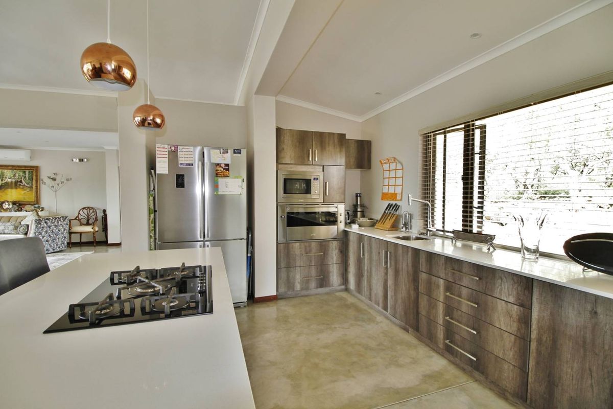 Modern kitchen featuring wood-grain cabinetry, stone countertops, a central island with a built-in gas hob, and integrated stainless steel appliances.