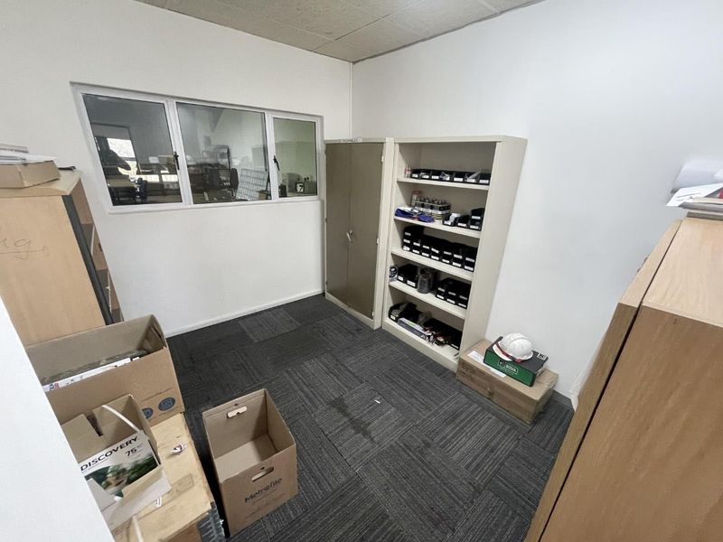 A functional office space featuring carpet tile flooring, a drop ceiling, and an internal window providing visibility into the adjacent area.