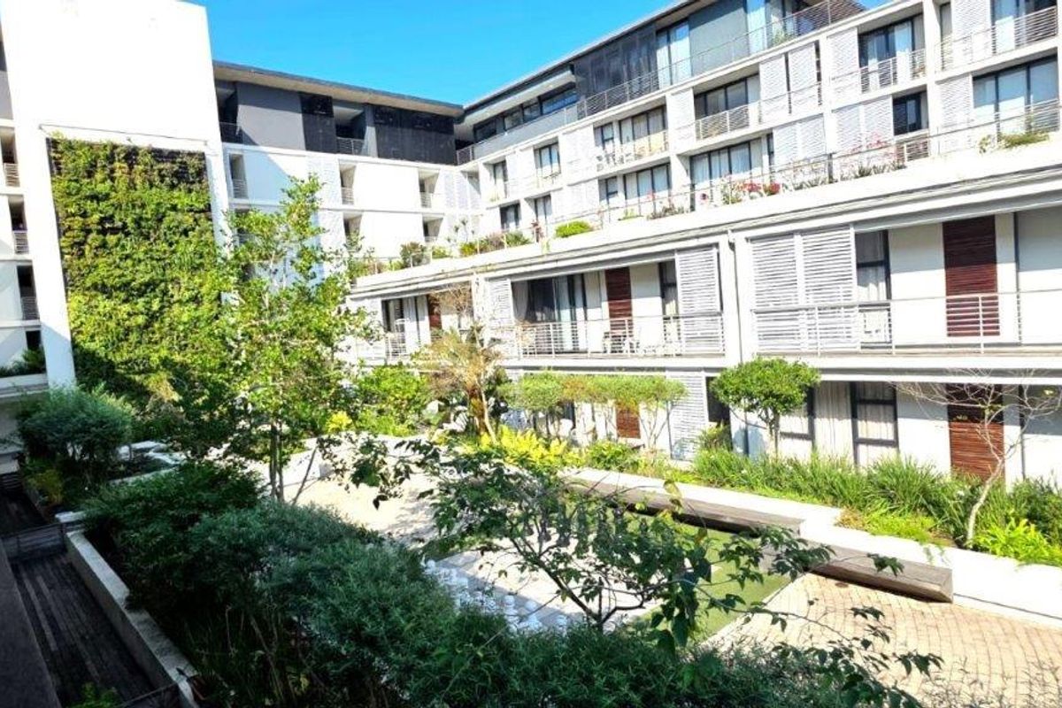 A well-maintained apartment complex courtyard featuring landscaped gardens, vertical greenery, paved walkways, and private balconies overlooking the central outdoor space.