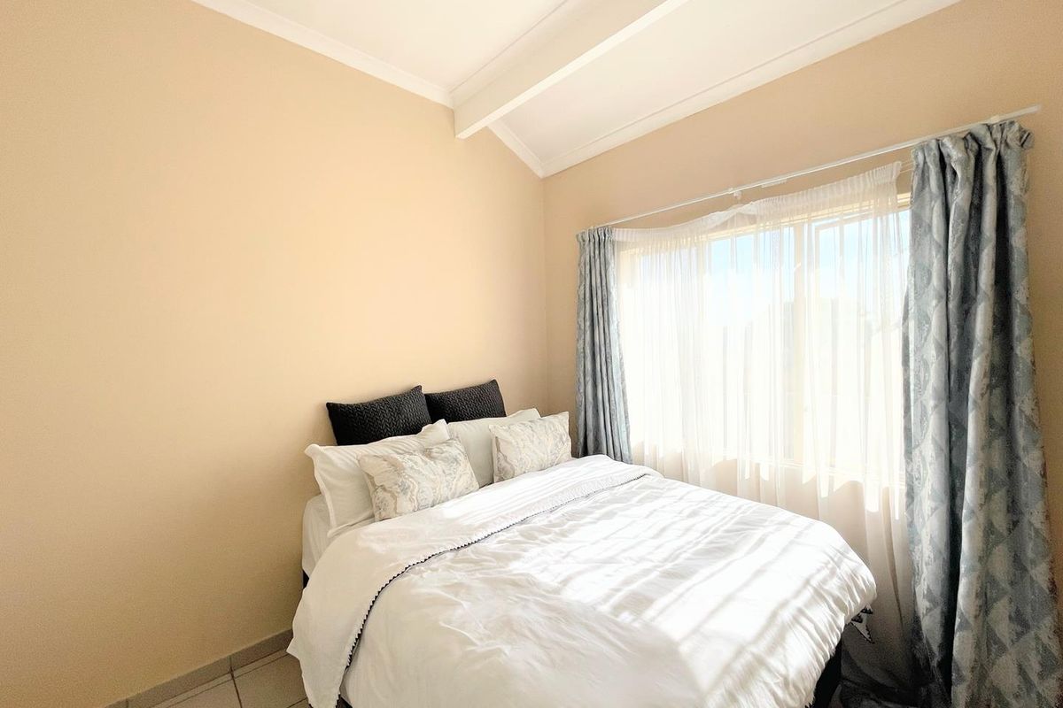 A bright bedroom featuring vaulted ceilings, tiled flooring, and a large window with natural light.