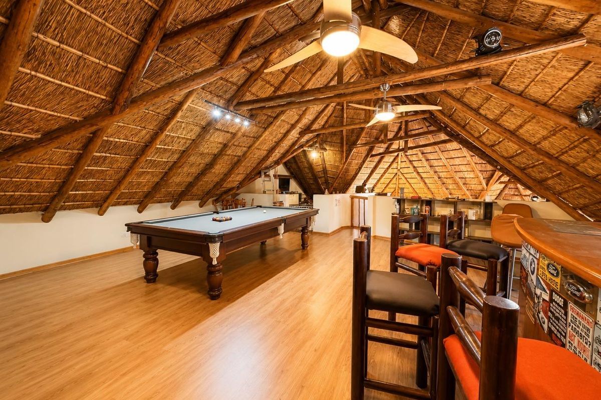 Spacious loft-style living area featuring a high vaulted thatched roof with exposed timber rafters, laminate flooring, and a built-in bar area.