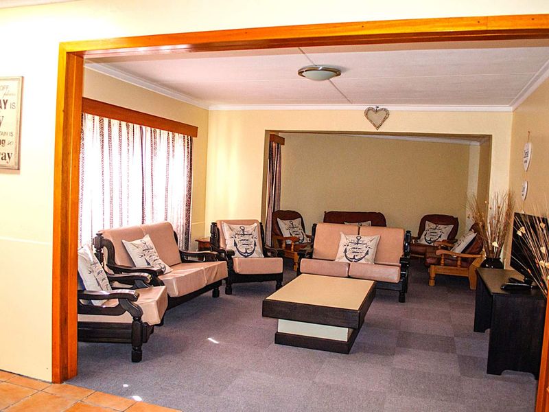 A spacious living area featuring carpeted flooring, neutral walls, and a prominent timber-framed opening connecting to an adjacent room.