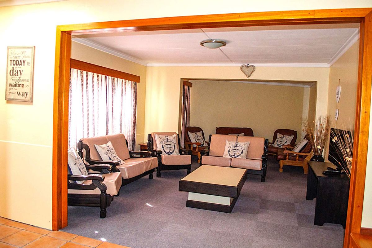 A spacious living area featuring carpeted flooring, neutral walls, and a prominent timber-framed opening connecting to an adjacent room.