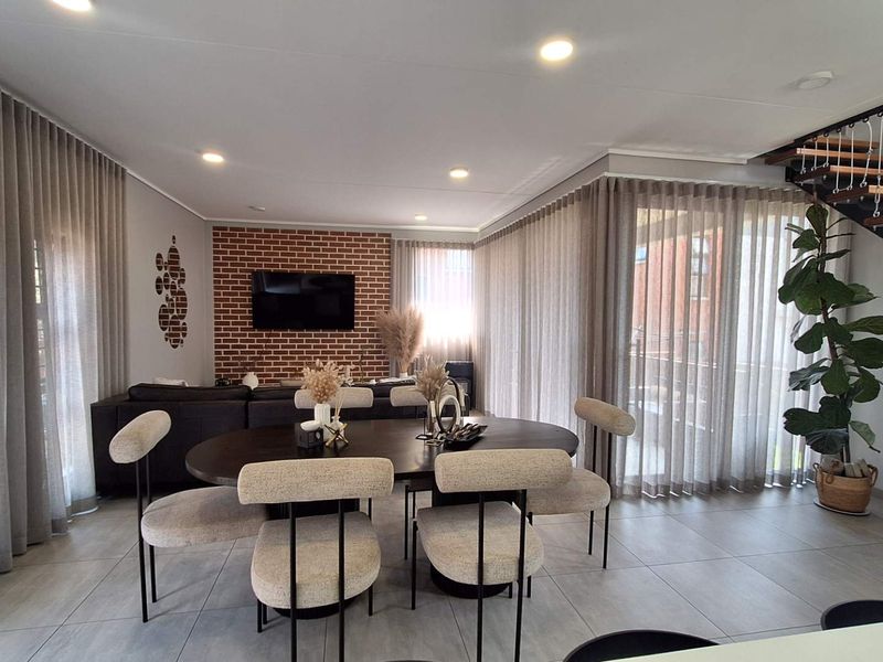 Spacious open-plan living and dining area featuring modern tiled floors, an exposed brick feature wall, and a contemporary staircase with a metal balustrade.