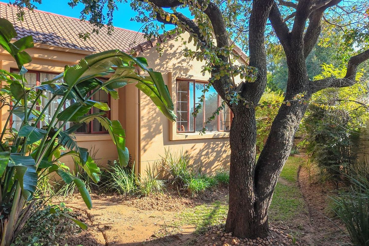 A view of the rear exterior facade featuring a tiled roof, brown window frames, and a mature garden setting.