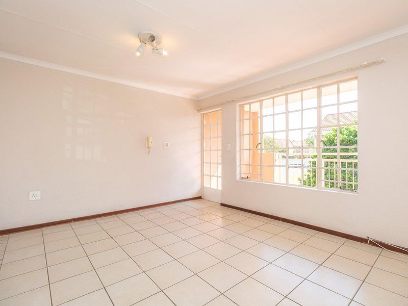 A bright, empty living room featuring neutral tiled flooring, a large grid-pattern window, and a glass-panel door leading to an outdoor area.