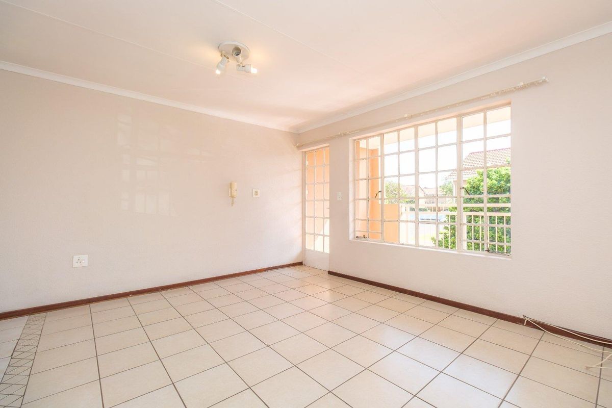 A bright, empty living room featuring neutral tiled flooring, a large grid-pattern window, and a glass-panel door leading to an outdoor area.