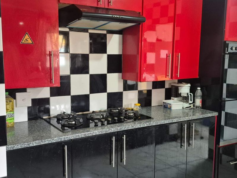 A kitchen featuring high-gloss red and black cabinetry, a black and white checkered tiled backsplash, granite countertops, and integrated cooking appliances.