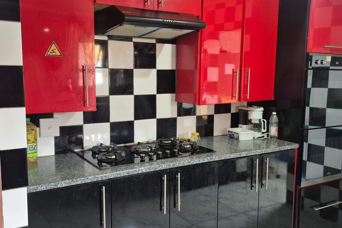 A kitchen featuring high-gloss red and black cabinetry, a black and white checkered tiled backsplash, granite countertops, and integrated cooking appliances.