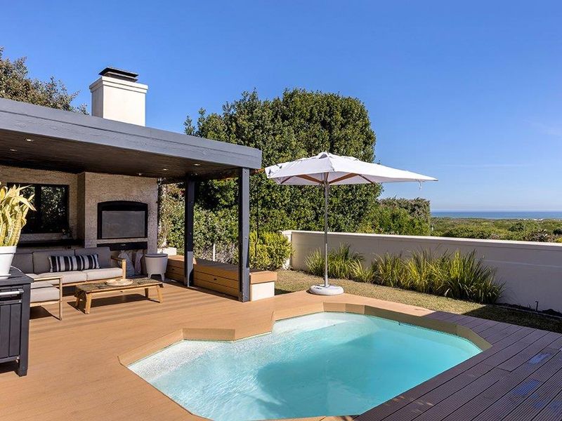 Outdoor entertainment area featuring a plunge pool, timber decking, and a built-in fireplace with scenic coastal views.
