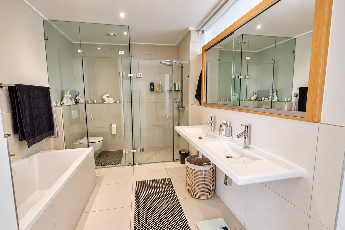 Modern bathroom featuring a double vanity, glass-enclosed shower, and a built-in bathtub with neutral tiling and high-quality fixtures.