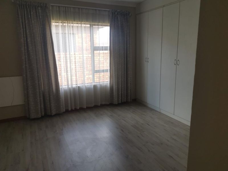 A bright, empty bedroom featuring light-toned laminate flooring and ample built-in cupboard storage space.