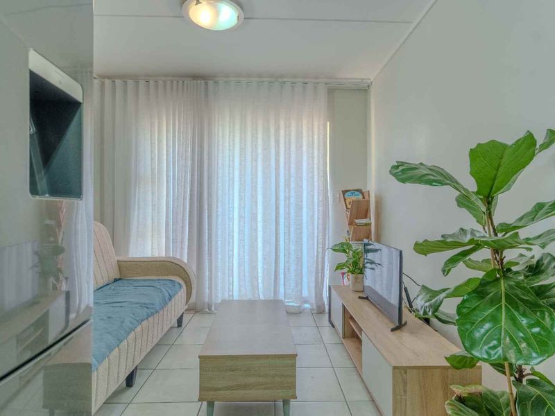 A compact living room featuring tiled flooring, neutral walls, and large windows dressed with floor-to-ceiling curtains, providing a bright and functional living space.