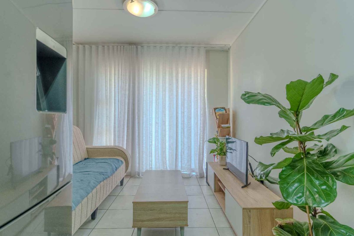 A compact living room featuring tiled flooring, neutral walls, and large windows dressed with floor-to-ceiling curtains, providing a bright and functional living space.