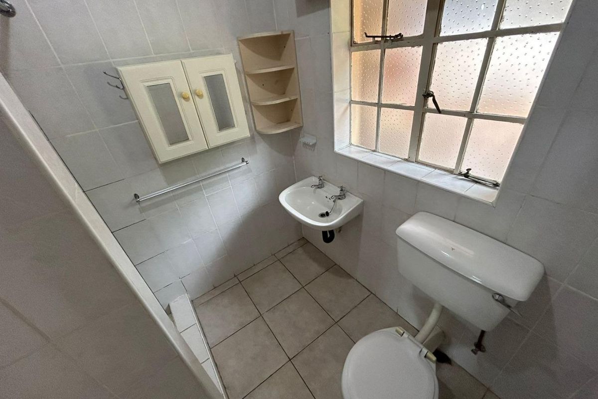 A compact bathroom featuring a wall-mounted basin, toilet, and tiled finishes, requiring modernization to improve its overall aesthetic and functionality.