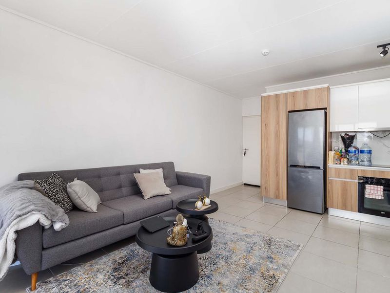 Modern open-plan living area featuring a sleek kitchen with wood-tone and white cabinetry, integrated oven, and neutral tiled flooring throughout.